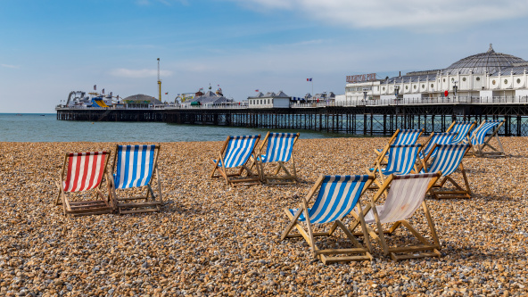 A view of Brighton Pier from the pebble beach with striped deckchairs in the foreground