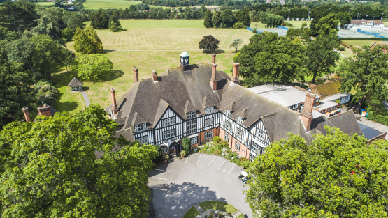 Exterior of Queenswoodtrew House surrounded by the school grounds which includes a sports area, fields, trees and a car park